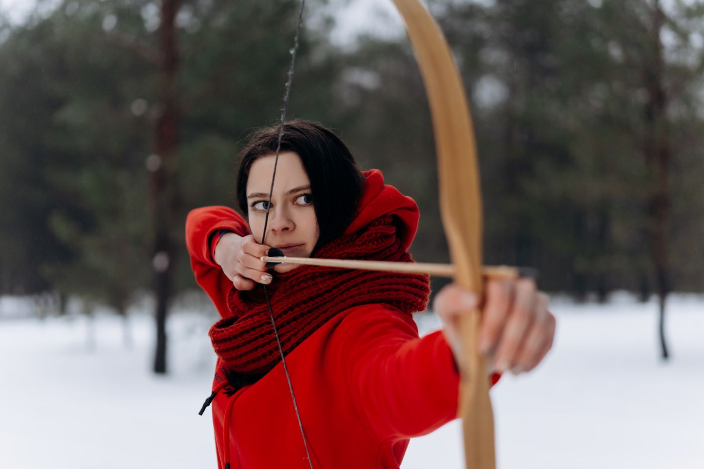 An archer at full draw with a long wooden bow, in falling snow